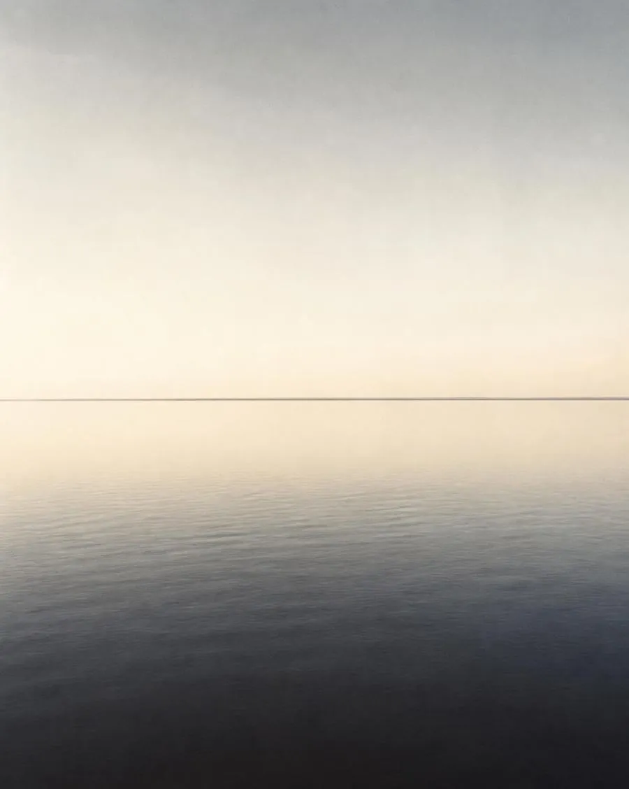 A still lake meeting a pale empty sky at the horizon line