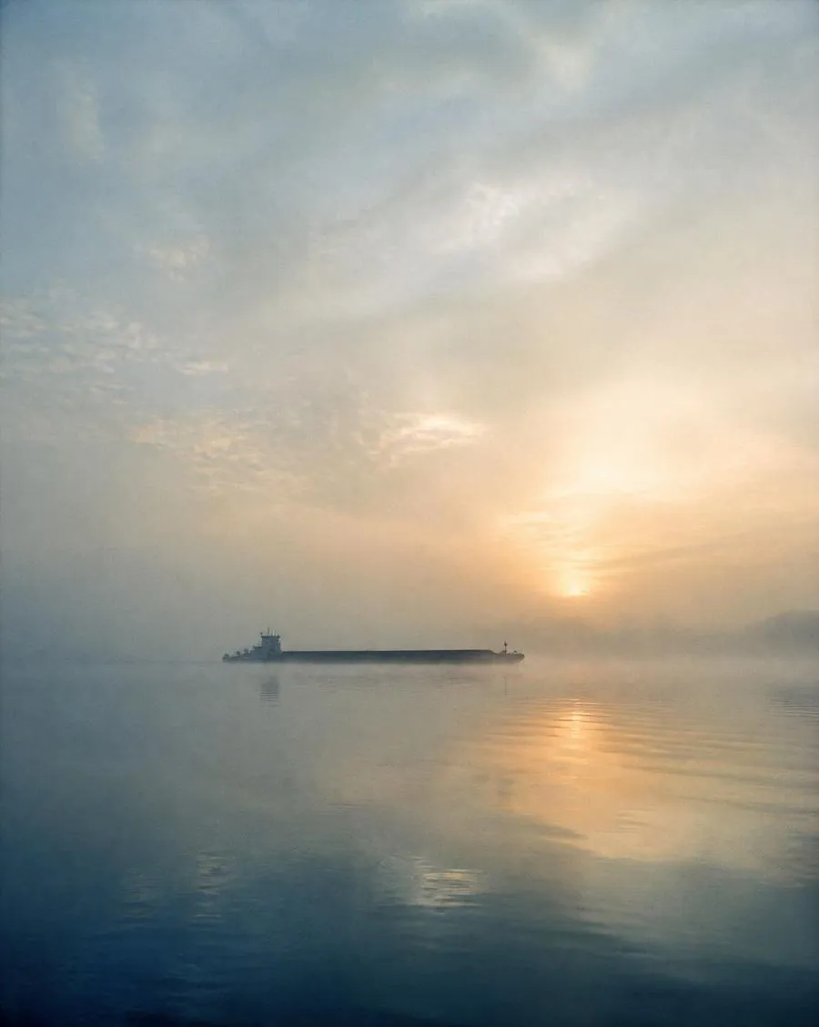 Mist rising off a wide river at dawn with a distant barge
