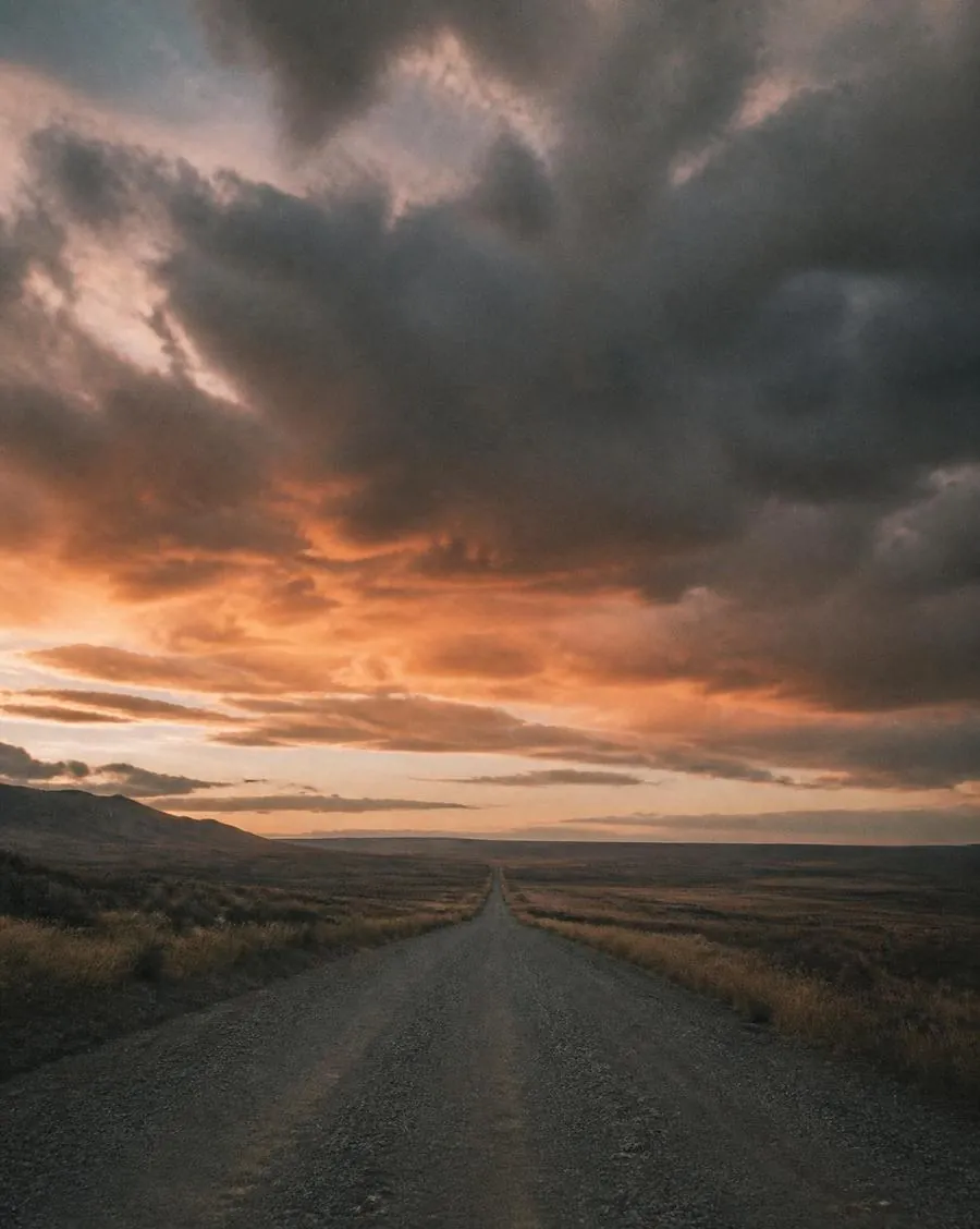 A gravel road vanishing into open plains beneath a dramatic sky